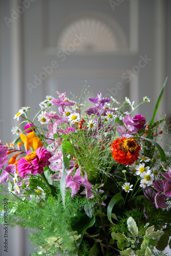 Stauß aus bunten Zinnien mit Kamille und Gräsern vor einer Holzwand