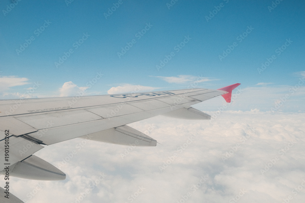 Fototapeta premium Airplane wing view above clouds with clear blue sky