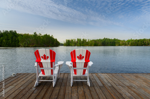 Fotografía Wide-angle view of two white Adirondack chairs with red maple leaf flags on a rustic dock