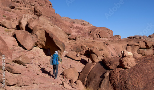 A male tourist in a trail in high mountains in Sinai next to town Saint Catherine. Red mountains and huge boulders of amazing forms. Vacation and hiking in Sinai.