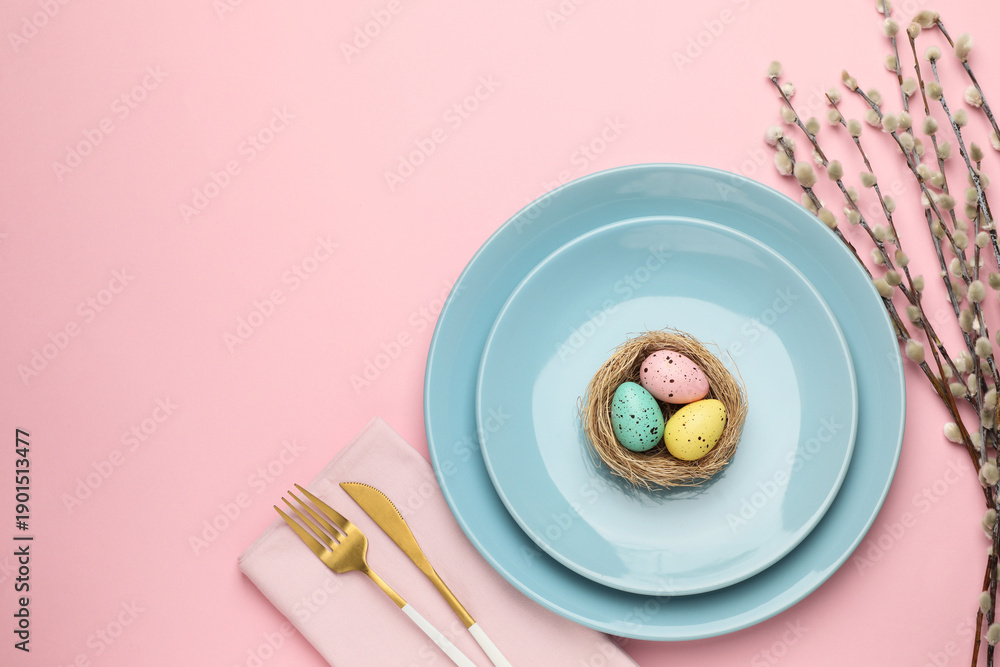 Fototapeta premium Easter celebration. Festive table setting with painted eggs, willow branches and cutlery on pink background, flat lay with space for text