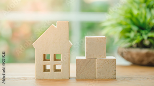 A miniature wooden house stands beside two stacked wooden blocks on a wooden surface