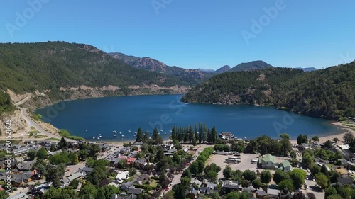 Aerial view of Lake Lacar and San Martin de los Andes in Patagonia, highlighting a scenic marina with numerous sailboats and boats anchored in deep blue water surrounded by mountains.
