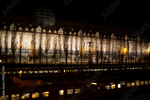 Foto Two night trains (both lit) passing in front of a long row of trees and identica