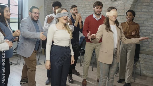 Young professionals playing trust game with blindfolds in office