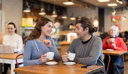 Tableau sur toile Couple are chatting happily with each other while sitting at table in a cafe and