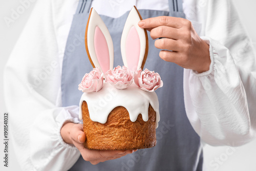 Photography Female confectioner holding delicious Easter cake with bunny ears and roses on w