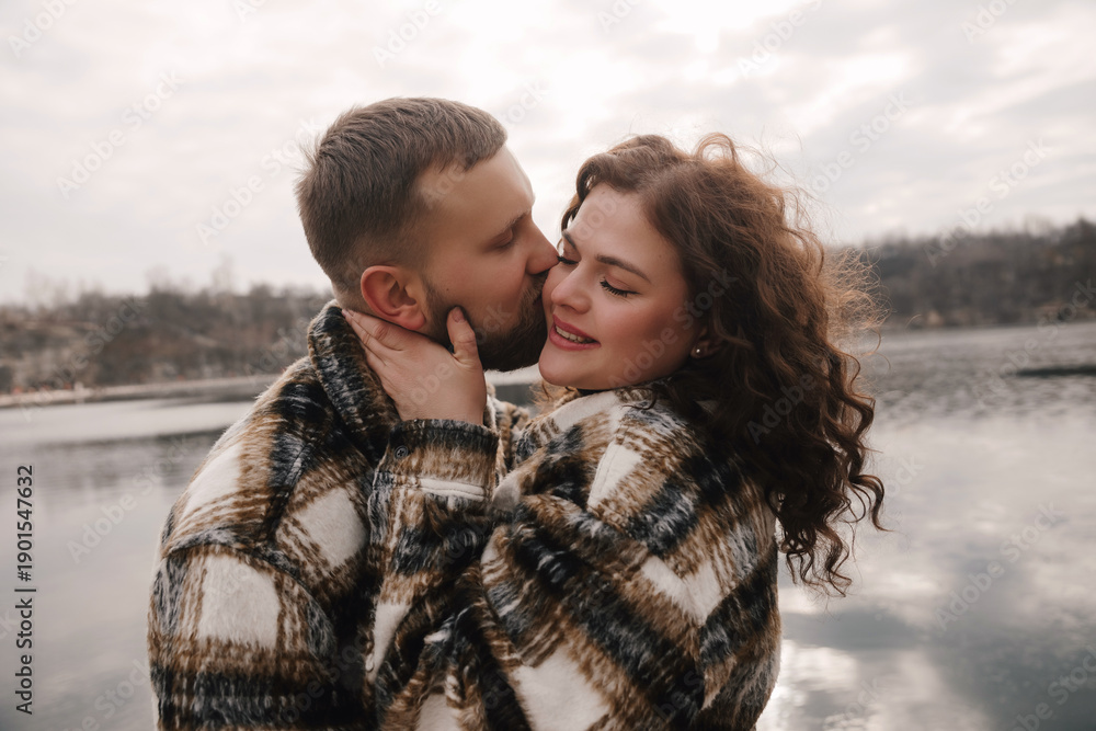 Fototapeta premium Couple shares a romantic moment outdoors on a cloudy day near a lake