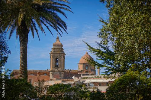 Foto Lush palm tree and dense greenery frame the bell tower and domed church in old town of Erice in Sicily