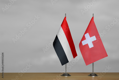 Two table flags of Yemen and Switzerland on a blurred gray background