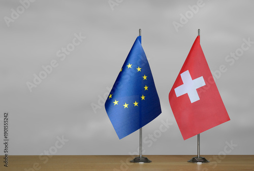 Two table flags of the European Union and Switzerland on a blurred gray background