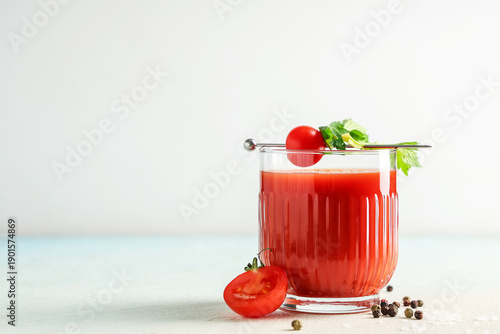 Glass of bloody mary with celery, tomatoes and peppercorns on light background