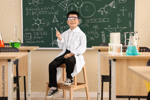 Cute little boy sitting on stepladder near chalkboard in chemistry classroom