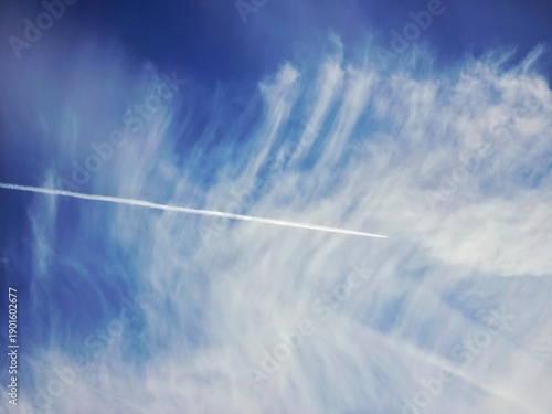 Passenger aircraft cruising at high altitude and high speed, leaving contrails behind, with a blue sky in the background.