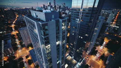 Night aerial view of modern city skyline with illuminated skyscrapers and streets. Urban architecture and cityscape details create a vibrant metropolitan atmosphere at dusk.