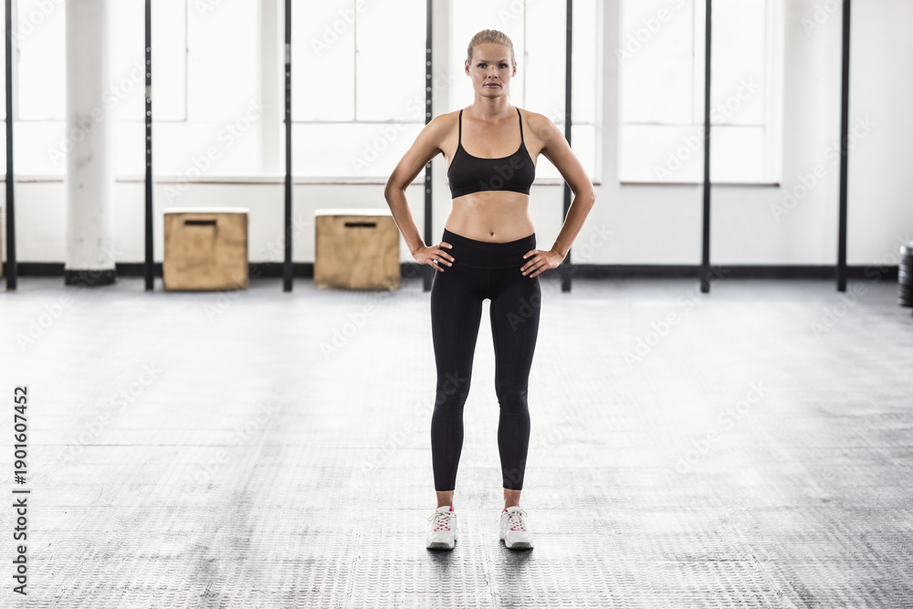 Obraz premium Woman standing centered in gym on rubber floor, wearing black bra and leggings near plyo boxes