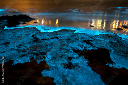 Foto Bioluminescent waves glowing blue around coastal rock platforms at night in Jervis Bay, New South Wales, Australia, with illuminated water and calm ocean conditions