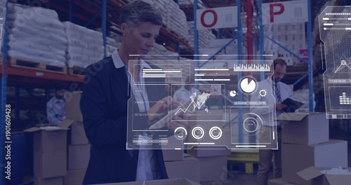 Obraz na plátne Supervising logistics supervisor wearing blazer tapping tablet in warehouse, wit