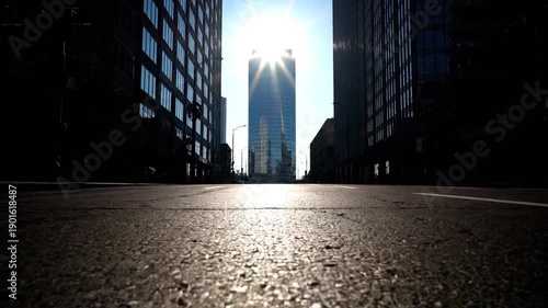 Low angle view of a modern skyscraper in a city street with sun flare