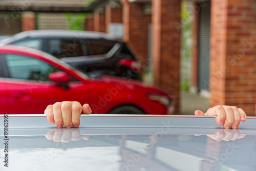 Child hands gripping white rail with red and black cars behind.