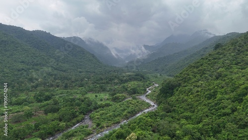 Lush Green Valley with Winding River and Misty Mountains on a Cloudy Day