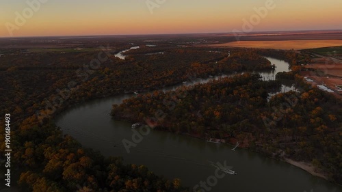 Trentham Cliffs follow the Murray River as evening colors deepen across the landscape, aerial pullback as boats navigate waterway