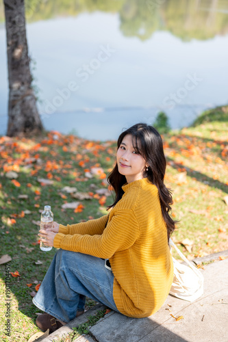 Obraz na płótnie Pretty asian woman holding water bottle while sits on sidewalk aside grass lawn