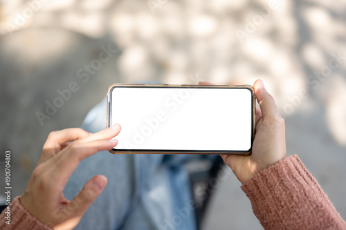 A woman's hand holding and touching white screen phone sitting on outdoor bench over concrete floor.