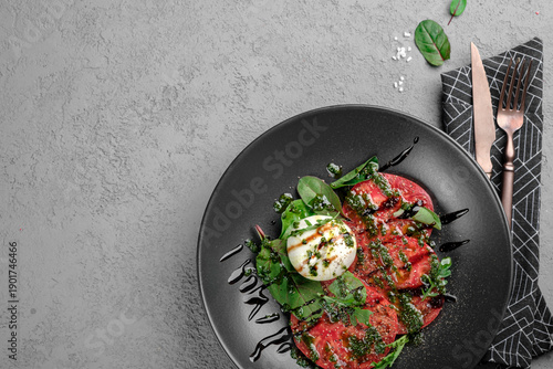 Obraz na płótnie Fresh tomato carpaccio with creamy burrata, pesto drizzle, fresh basil leaves and balsamic glaze on black plate