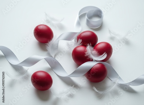 Elegant Easter eggs in red, adorned with delicate white feathers and silver ribbon, on a clean white background.