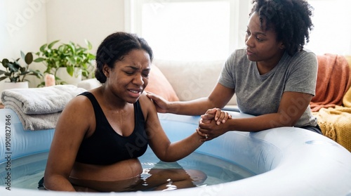 African american doula aiding young mother in water birth. Expectant mother finds comfort from caring doula during natural labor, peaceful water birth. Promoting maternal health, informed choices,