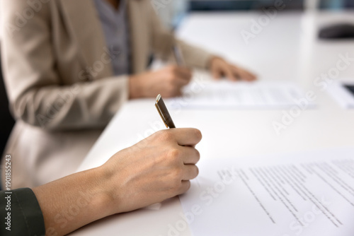 Photography Close up of two women, business parties concluding agreement, closing commercial deal, seated at conference table, signing official documents