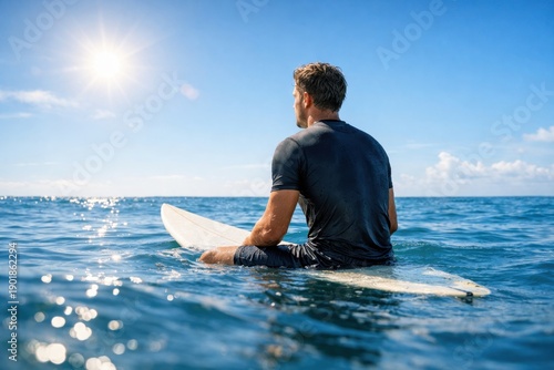 Surfer sitting on surfboard in calm ocean water under bright sun enjoying peaceful summer day at sea