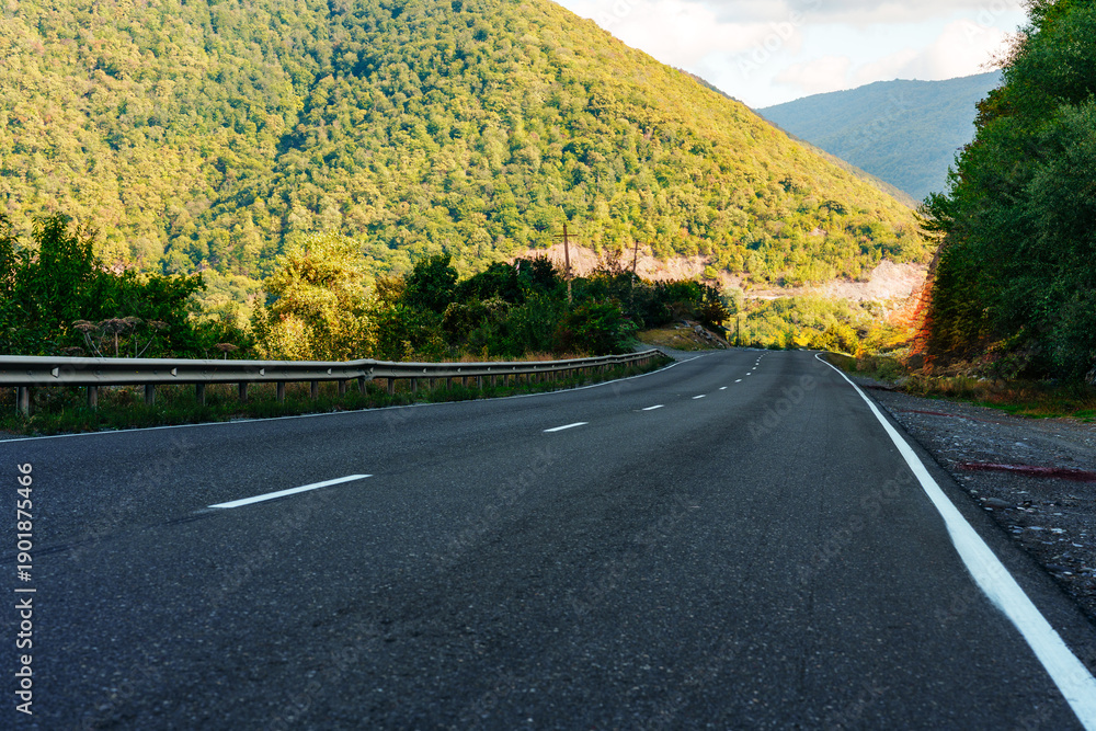 Fototapeta premium Driving on a winding road through green mountains near a forest in daylight