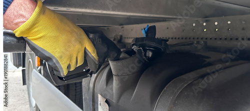 Foto Worker wearing yellow gloves refuels a large vehicle using a fuel nozzle, with a