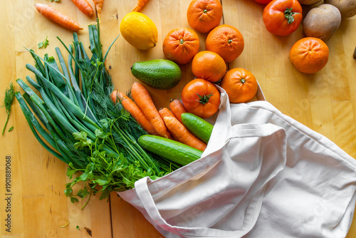 Fresh vegetables and fruits in reusable cotton bag on wooden table. Eco shopping, healthy food, sustainable lifestyle, zero waste concept, seasonal spring and summer groceries.