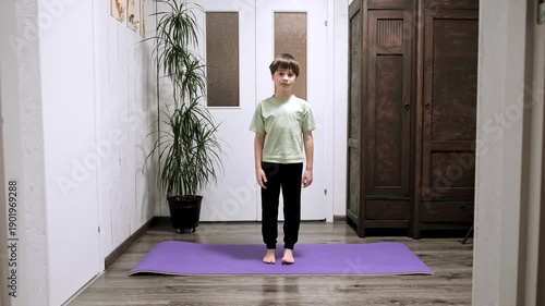 Boy doing exercise lifting on toes standing on yoga mat. Home workout concept. Schoolboy does calf raises during morning workout routine. Sporty lifestyle. High quality 4k footage.
