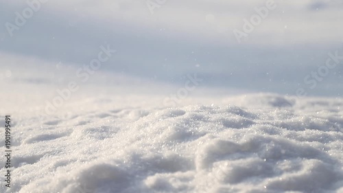 Close-up of glittering snowflakes blowing over a pristine snowy ground on a sunny winter day