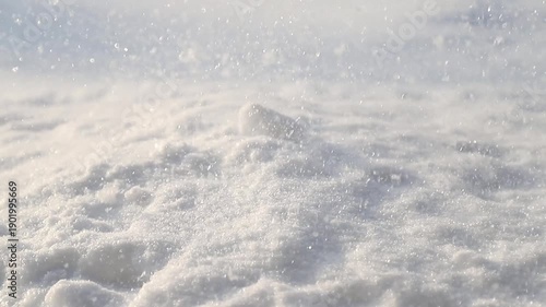 Close-up of glittering snowflakes blowing over a pristine snowy ground on a sunny winter day
