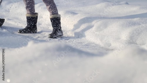 Close-up of a person wearing winter boots and shoveling a path in the snow on a sunny day