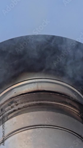 Winter scene of a small wooden house with snow on the roof and a silver chimney releasing wood smoke into clear blue sky