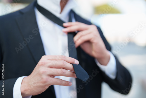 Fotografía Man is carefully adjusting a black necktie over a white shirt, preparing for a w