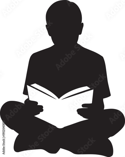Silhouette of a young boy sitting cross-legged and engrossed in reading a book