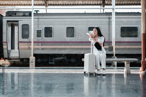 Woman sitting on a bench at a train station with luggage, ready for travel. Train in the background.