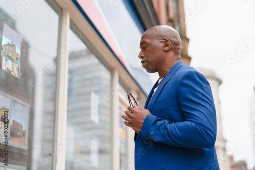 Man in blue suit looks at property listings in city window during afternoon