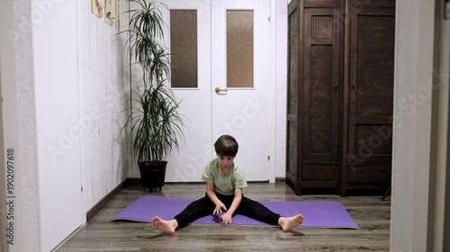 9 year old boy doing a seated forward bend stretch to limber up his hamstrings before starting home exercise routine. Child practicing flexibility. Healthy lifestyle concept. High quality 4k footage.
