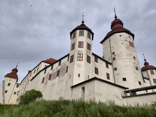 Lacko Castle, Sweden - August 29th 2024: View of Lacko Castle featuring white stone walls, round towers with red roofs and an arched entrance under an overcast sky in Sweden