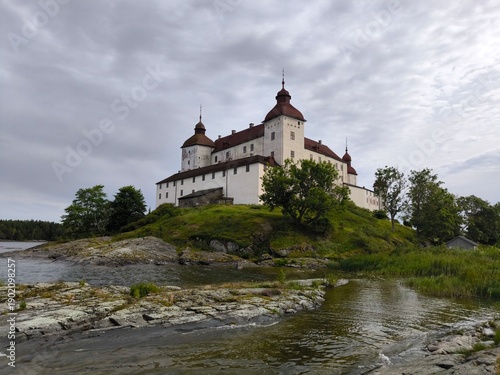 Lacko Castle, Sweden - August 29th 2024: View of Lacko Castle featuring white stone walls, round towers with red roofs and an arched entrance under an overcast sky in Sweden