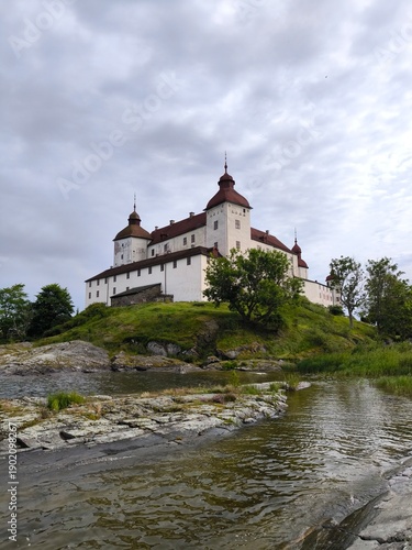 Lacko Castle, Sweden - August 29th 2024: View of Lacko Castle featuring white stone walls, round towers with red roofs and an arched entrance under an overcast sky in Sweden