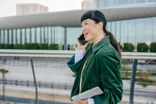 Confident businesswoman talking on mobile phone outdoors holding tablet